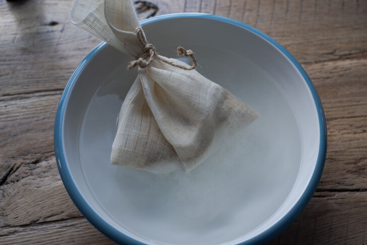 A linen pouch holding malt barley in a bowl of water to make sikhye.