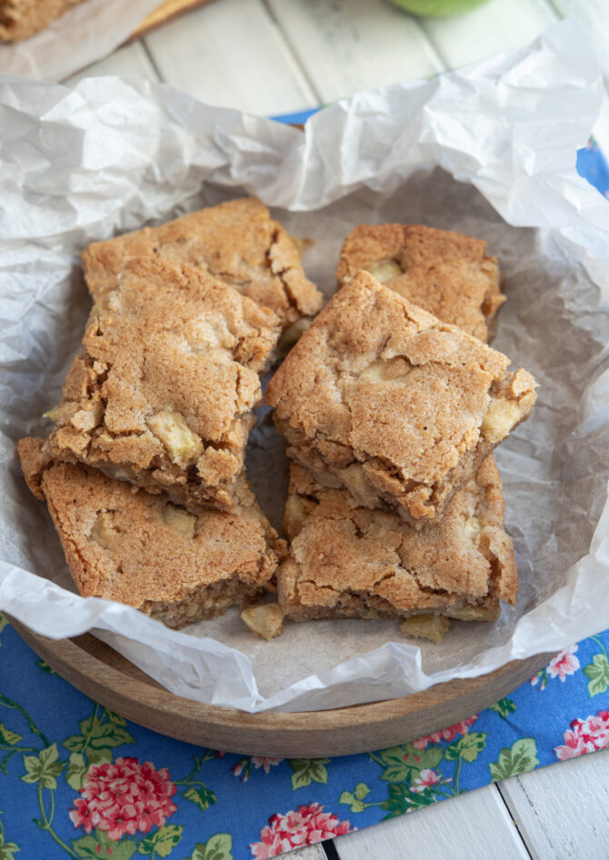 Slices of apple brownies are placed in a bowl lined with white parchment paper.