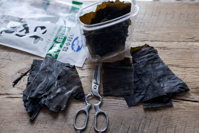 Dried sea kelp (kombu) is cut with scissor and stored in a jar.