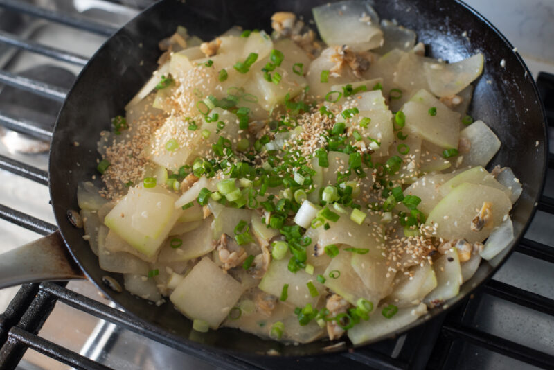 Green onion and toasted sesame seeds are added to cooked winter melon in a skillet.