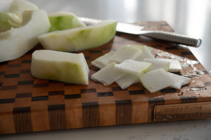 Peeled winter melon is thinly sliced on the cutting board.