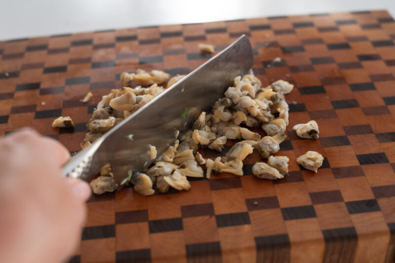 Clam meats are being chopped with a knife on the cutting board.