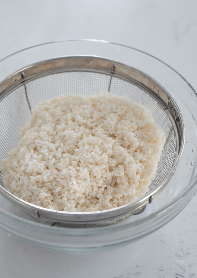 Soaked sweet rice is drained in a colander to discard the water.