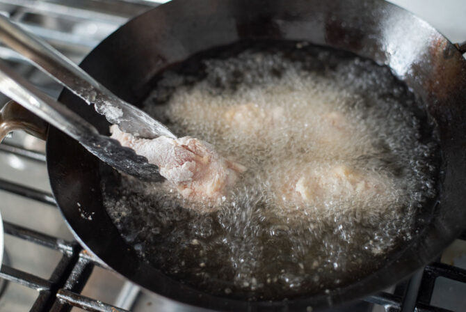Coated chicken wings enters hoil oil for deep frying.