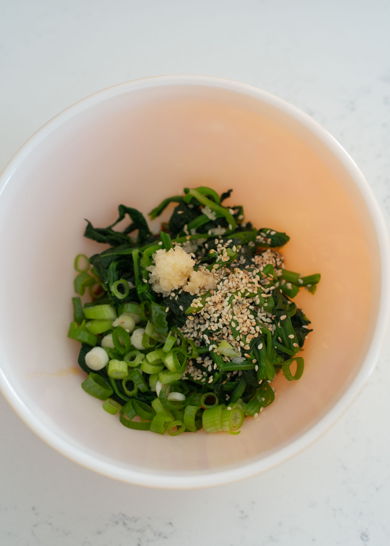 Blanched spinach is combined with Korean soy sauce seasoning in a bowl.