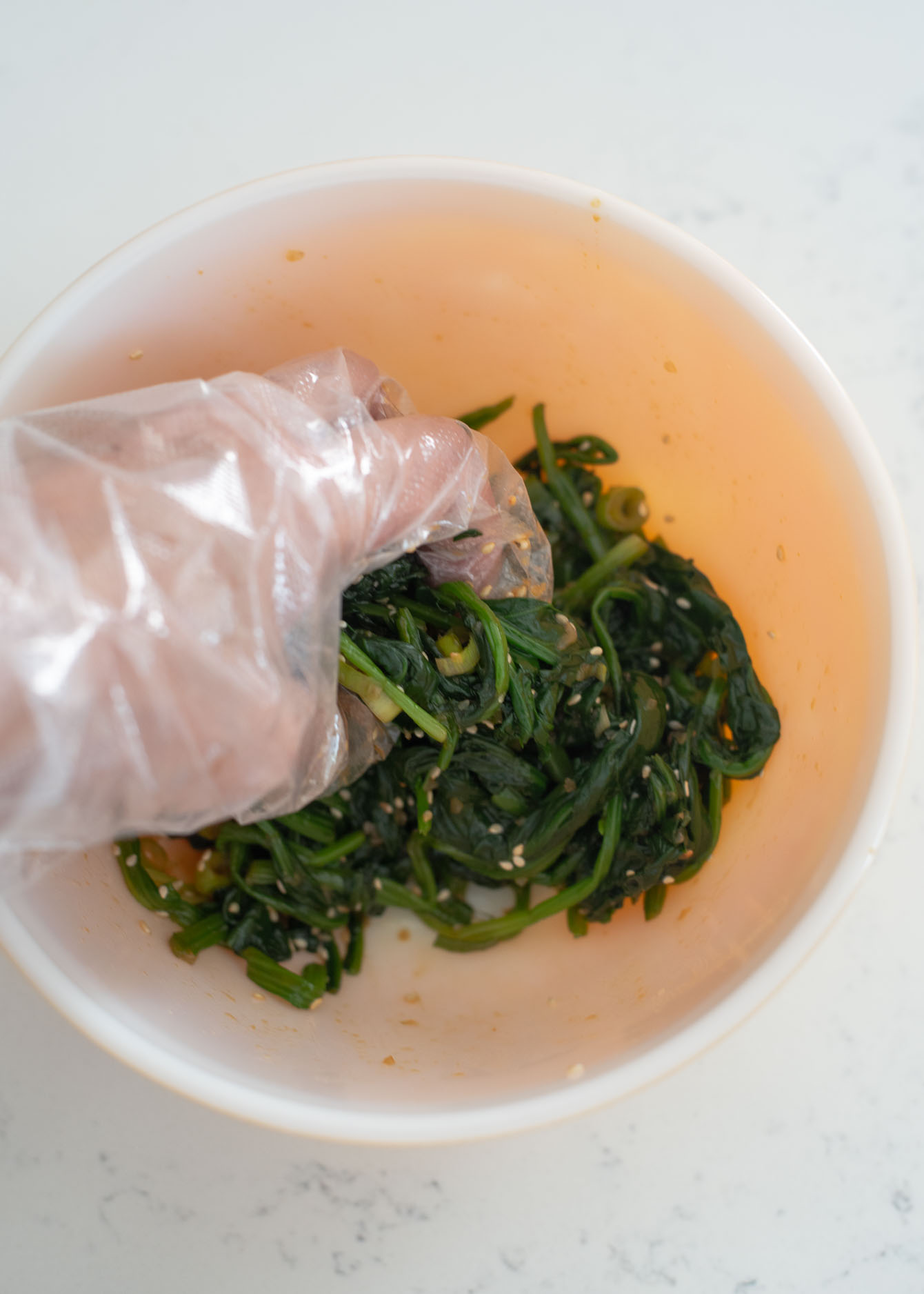 A bowl of blanched spinach is hand tossed to make Korean spinach side dish