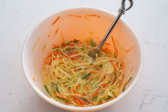 Shredded vegetables are mixed with beaten eggs in a bowl.