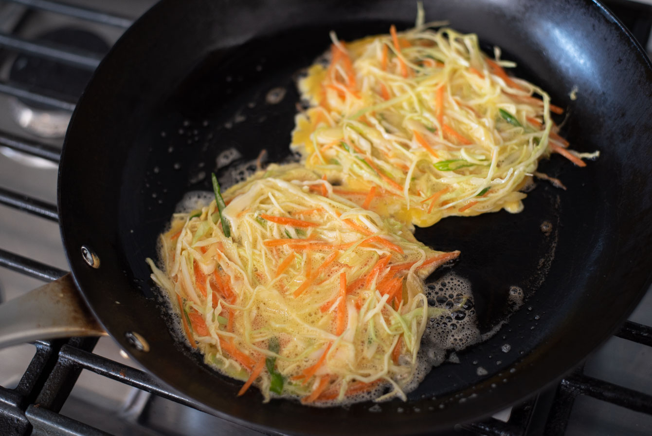 Two portions of egg omelette mixture cooking in a pan.