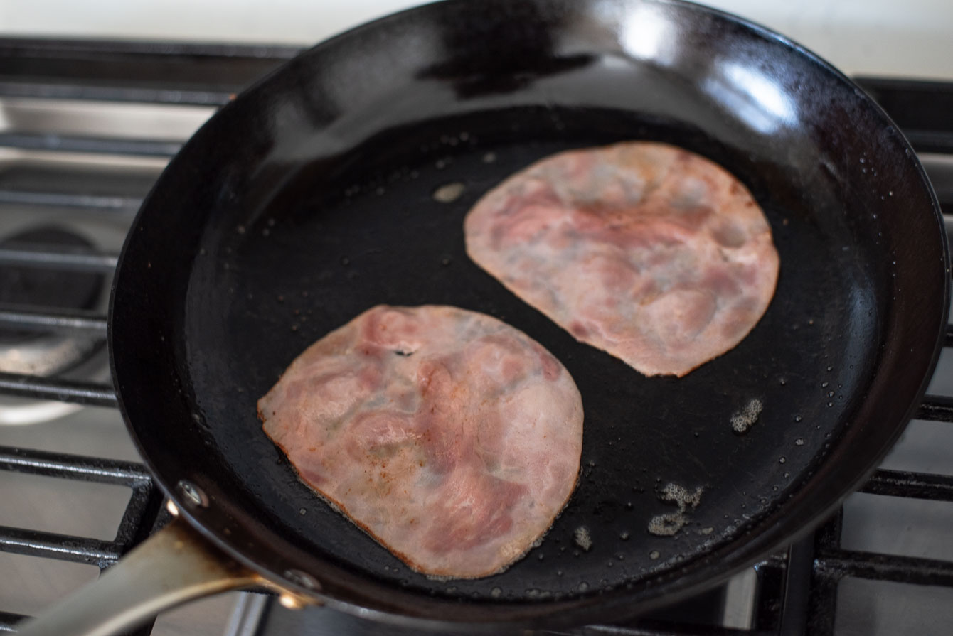 Two slices of deli ham heating in a skillet.