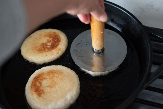A hotteok press is flattening hotteok dough in a griddle
