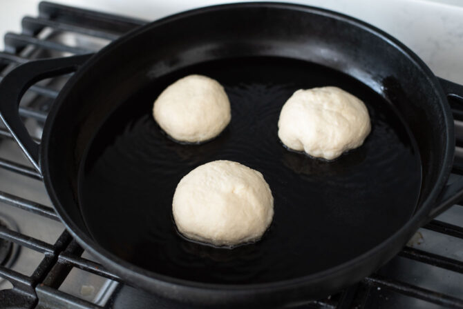 Three hotteok dough is placed on a hot griddle to fry.