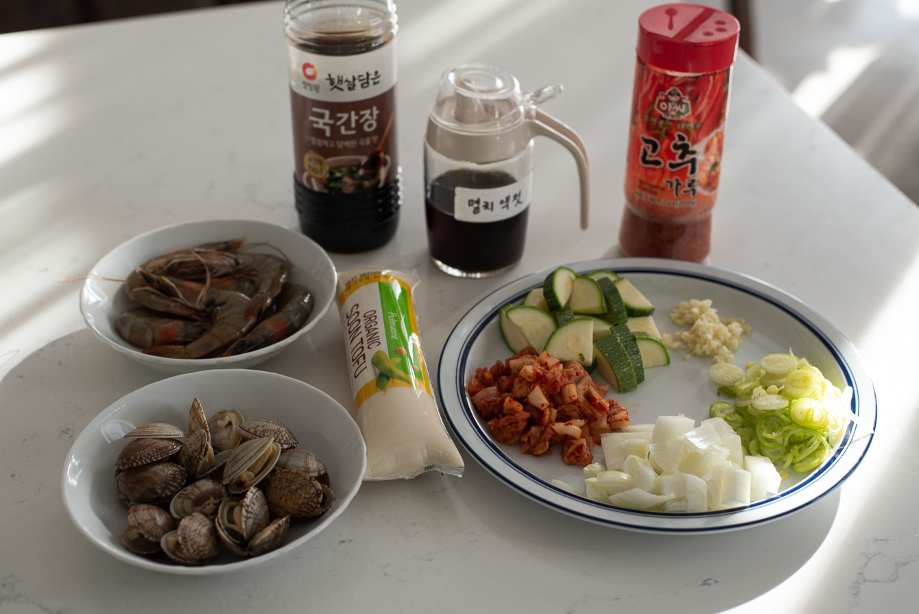 Ingredients laid out for sundubu jjigae including tofu, clams, shrimp, kimchi, and gochugaru
