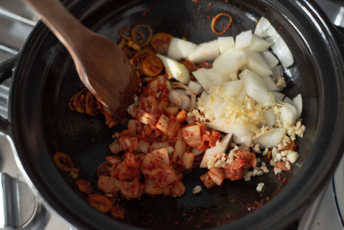 Onion, garlic, and kimchi is added to infused chili oil for making spicy tofu soup.