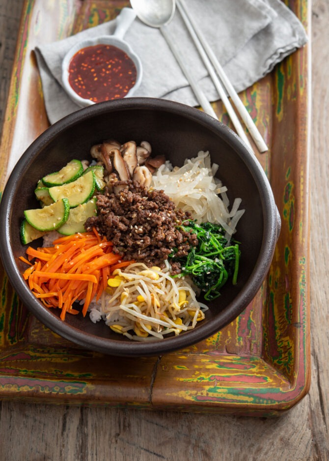 Various vegetables and ground beef bulgogi are arranged over rice in a stone bowl to make bibimbap
