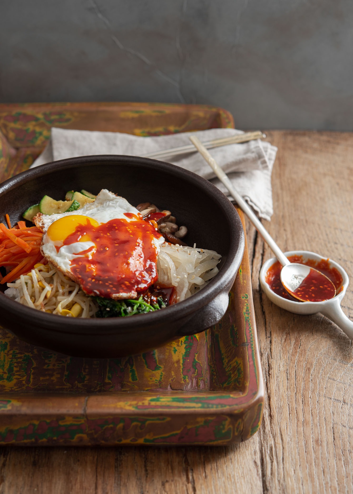 A bowl of Korean bibimbap on a tray is drizzled with gochujang sauce.