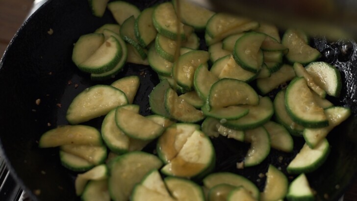 Stir-fried, soft zucchini slices in a skillet.