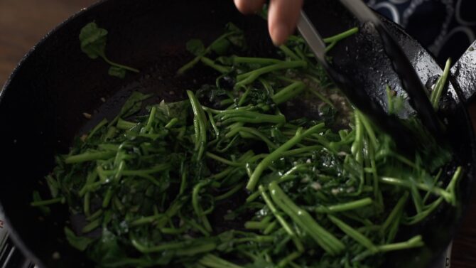 Green watercress are stir-fried in a skillet
