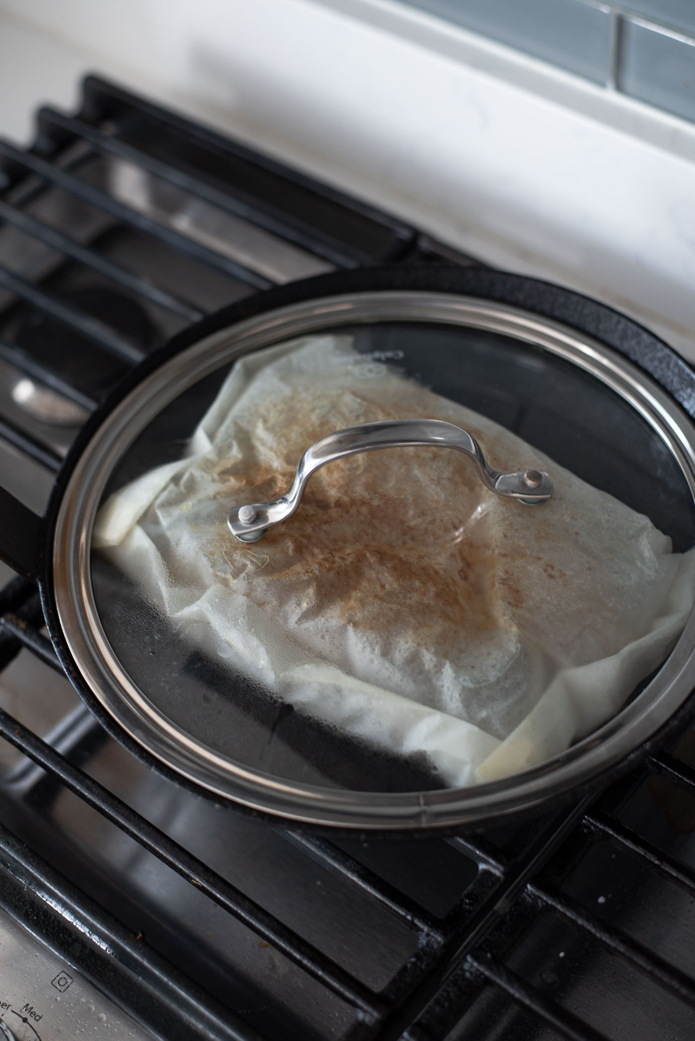 Mackerep fish in a parchment pouch is covered with a lid to continue to grill in a pan