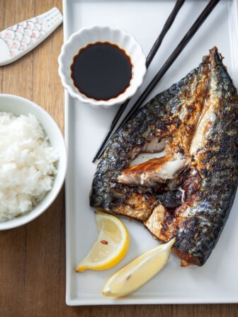 Grilled mackerel is served with soy sauce and lemon wedges in a white plate