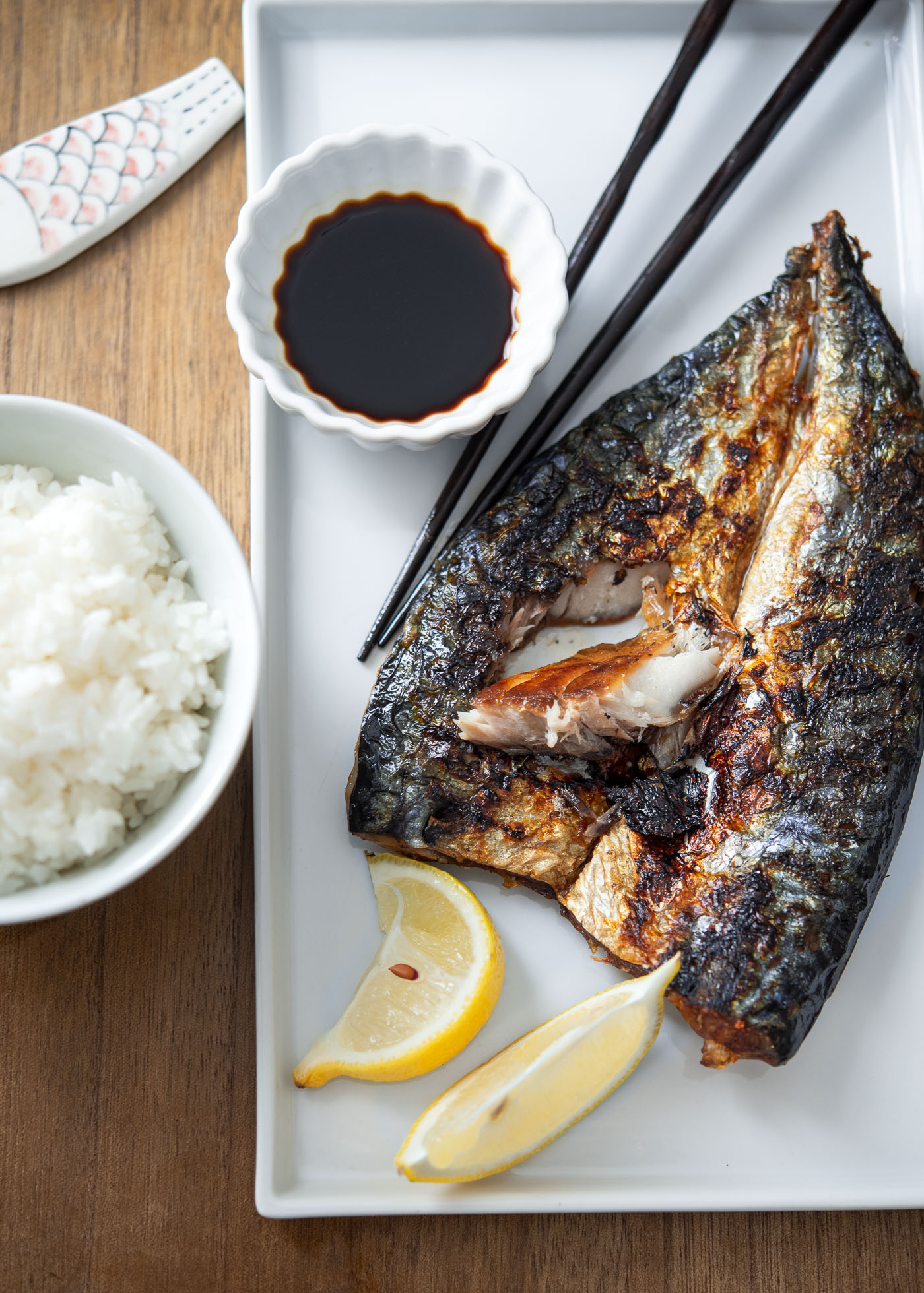 Grilled mackerel fish served with soy sauce and lemon wedges.