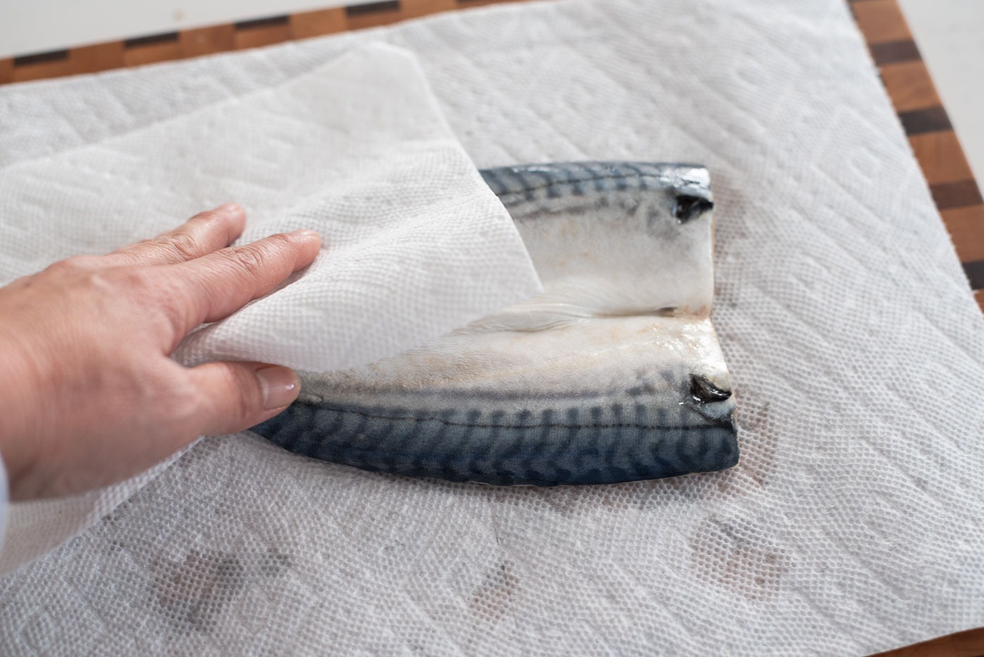 A piece of paper towel is used to wipe off the remaining moisture of mackerel filletss