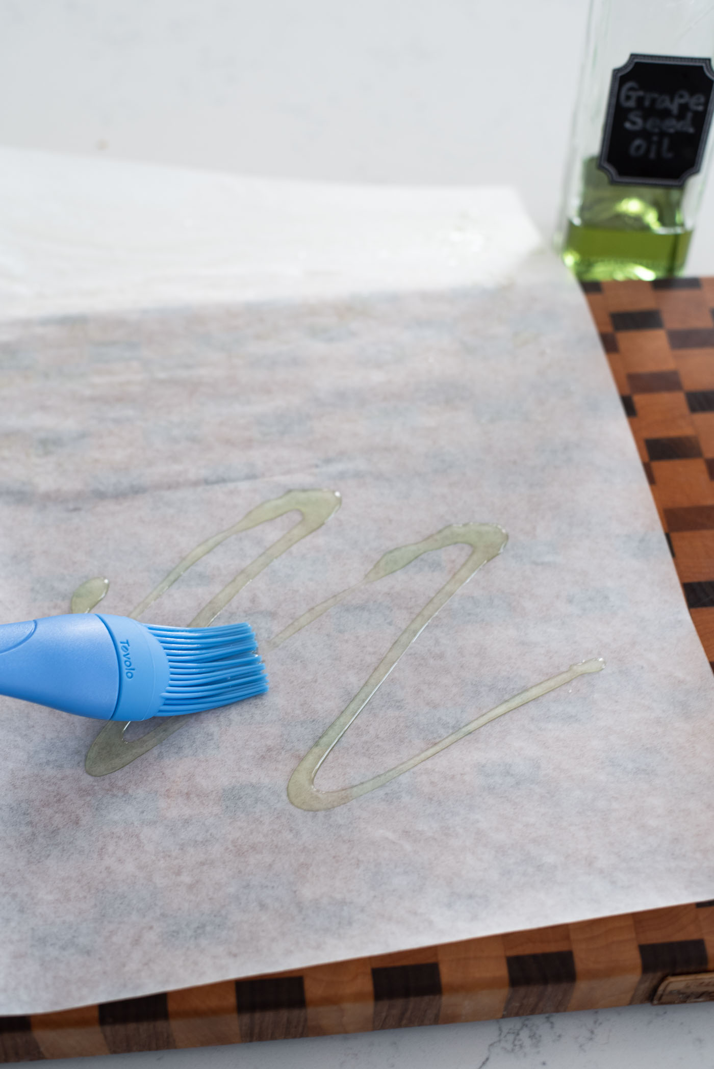 A blue brush is applying oil on a white parchment paper