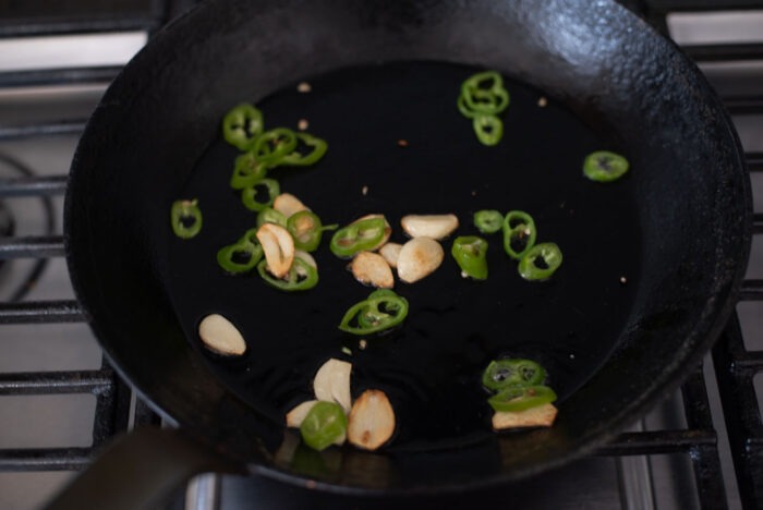 garlic slices and green chili pieces are cooked in a skilllet
