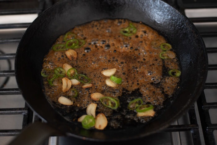 Garlic slices and green chili slices are cooking with a soy sauce mixture in a skillet