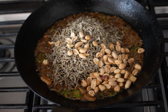 Tiny dried anchovies and peanuts are added to the sauce in a skillet