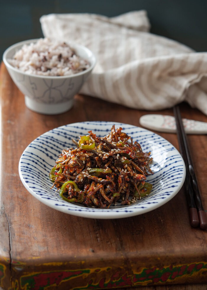 Small dried anchovy dish made with gochujang is on a blue plate and served with rice