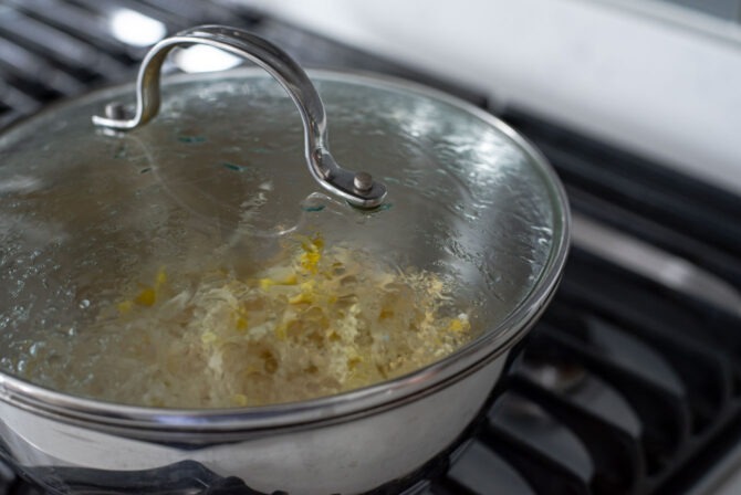 Bean sprouts are cooking in a pan covered with a lid.