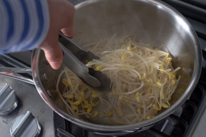 A kitchen tong is tossing cooked bean sprouts in a pot.