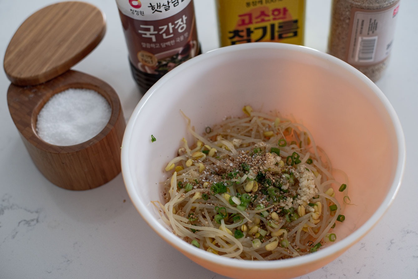 Cooked soybean sprouts are put in a bowl with green onion and other seasonings.