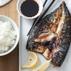 Grilled mackerel is served with soy sauce and lemon wedges in a white plate
