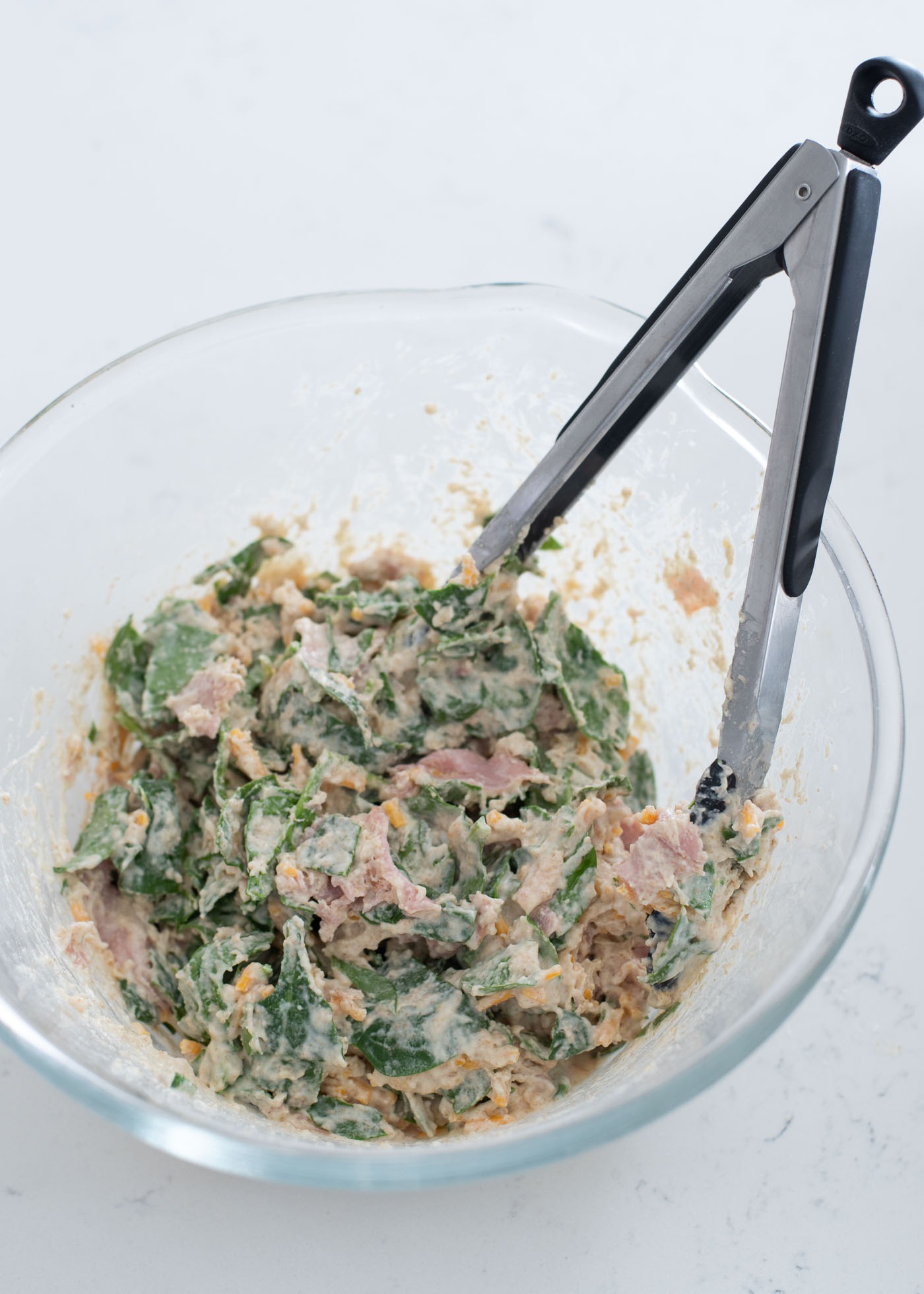Tossing savory waffle batter with spinach, ham, and cheese with kitchen tongs