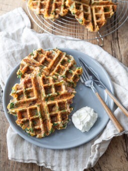 Savory waffles with spinach, ham and cheese are served on a blue plate with sour cream