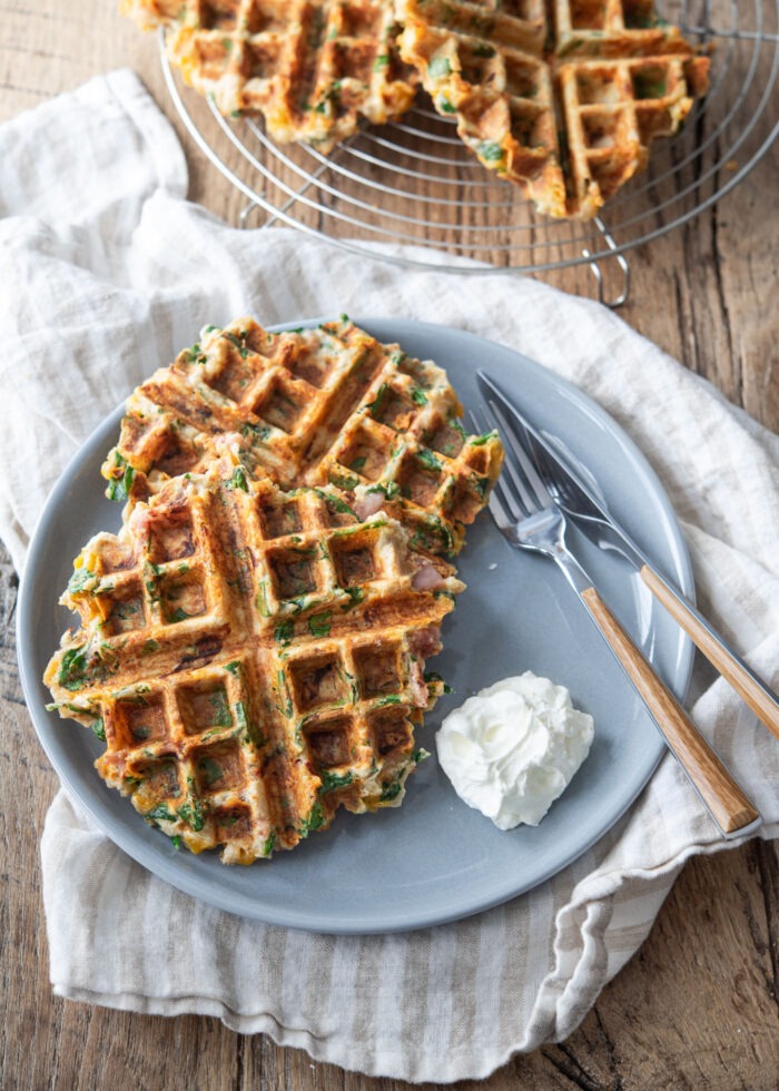 Savory waffles with spinach, ham and cheese are served on a blue plate with sour cream