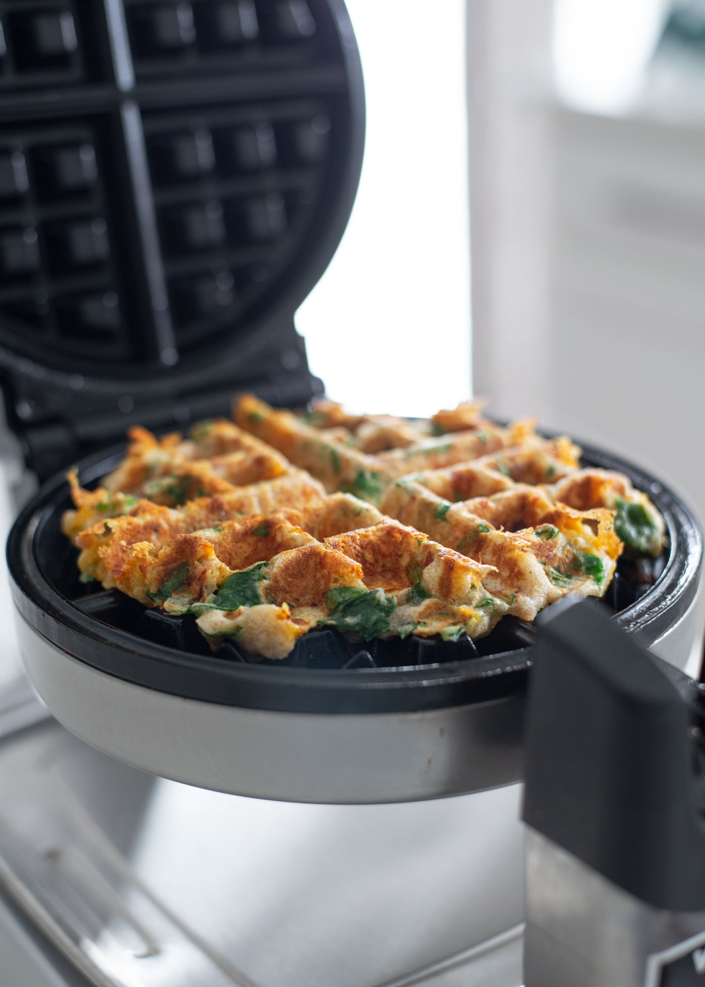 Savory waffles are finished cooking in a waffle maker to golden crisp.