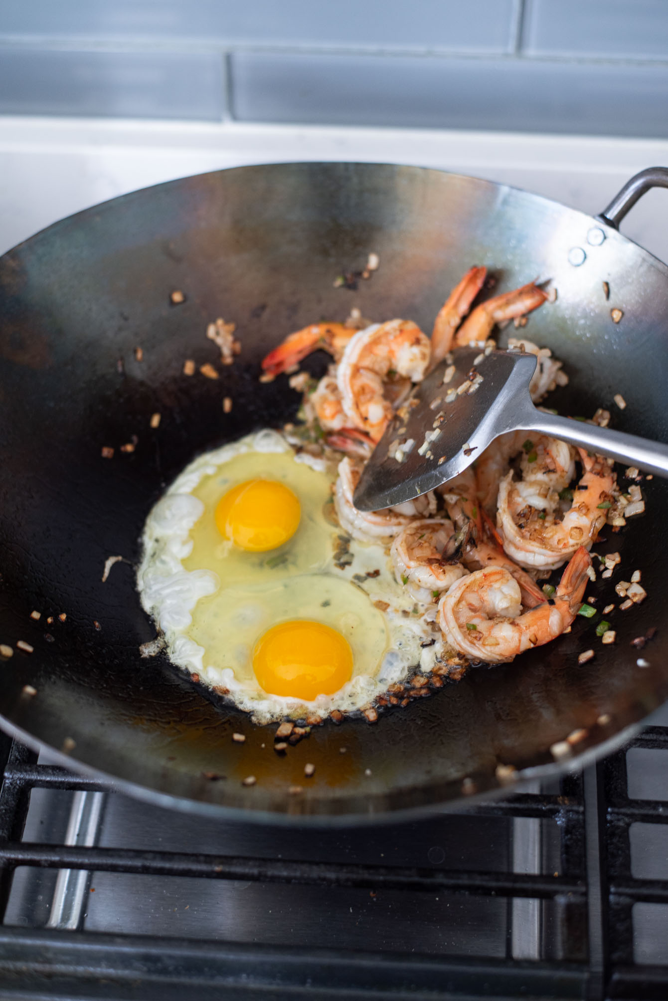 Two eggs are added to the shrimp in a wok