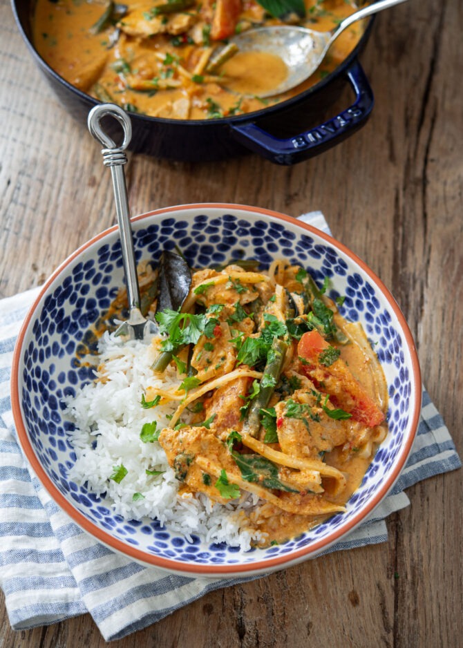 Thai red curry with chicken and vegetables is served over rice in a blue bowl