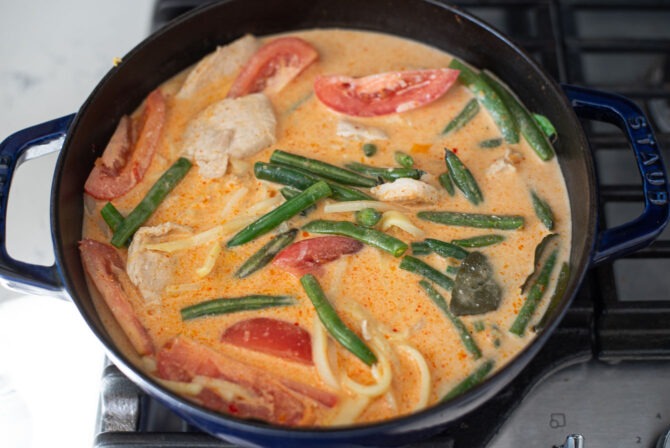 Coconut milk is added to chicken and vegetables in a pot