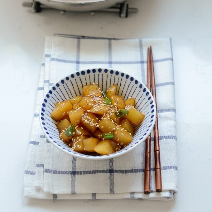 Cubes of Korean potato side dish is on a napkin with a pair of chopsticks