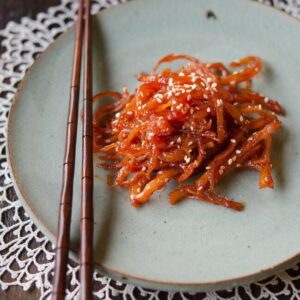 Korean shredded squid side dish is on a greet plate with a pair of chopsticks.