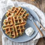 Savory waffles with spinach, ham and cheese are served on a blue plate with sour cream