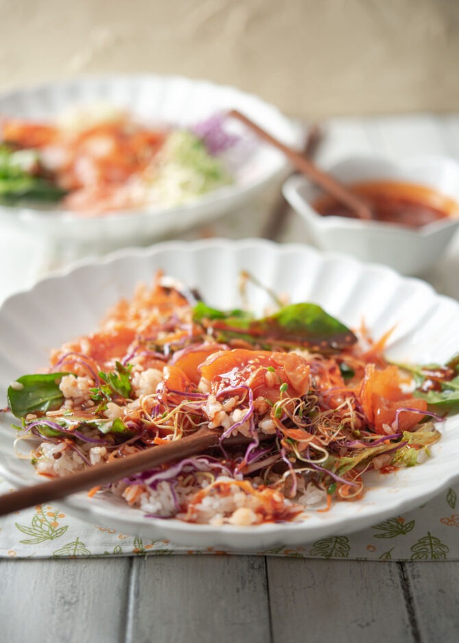 Salmon bibimbap is mixed together with salad green and sprouts in gochujang sauce 