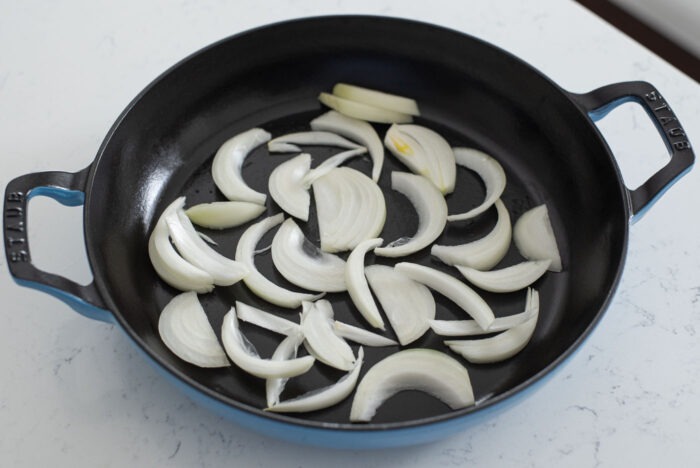 Sliced onion is placed on the bottom of large shallow pan.