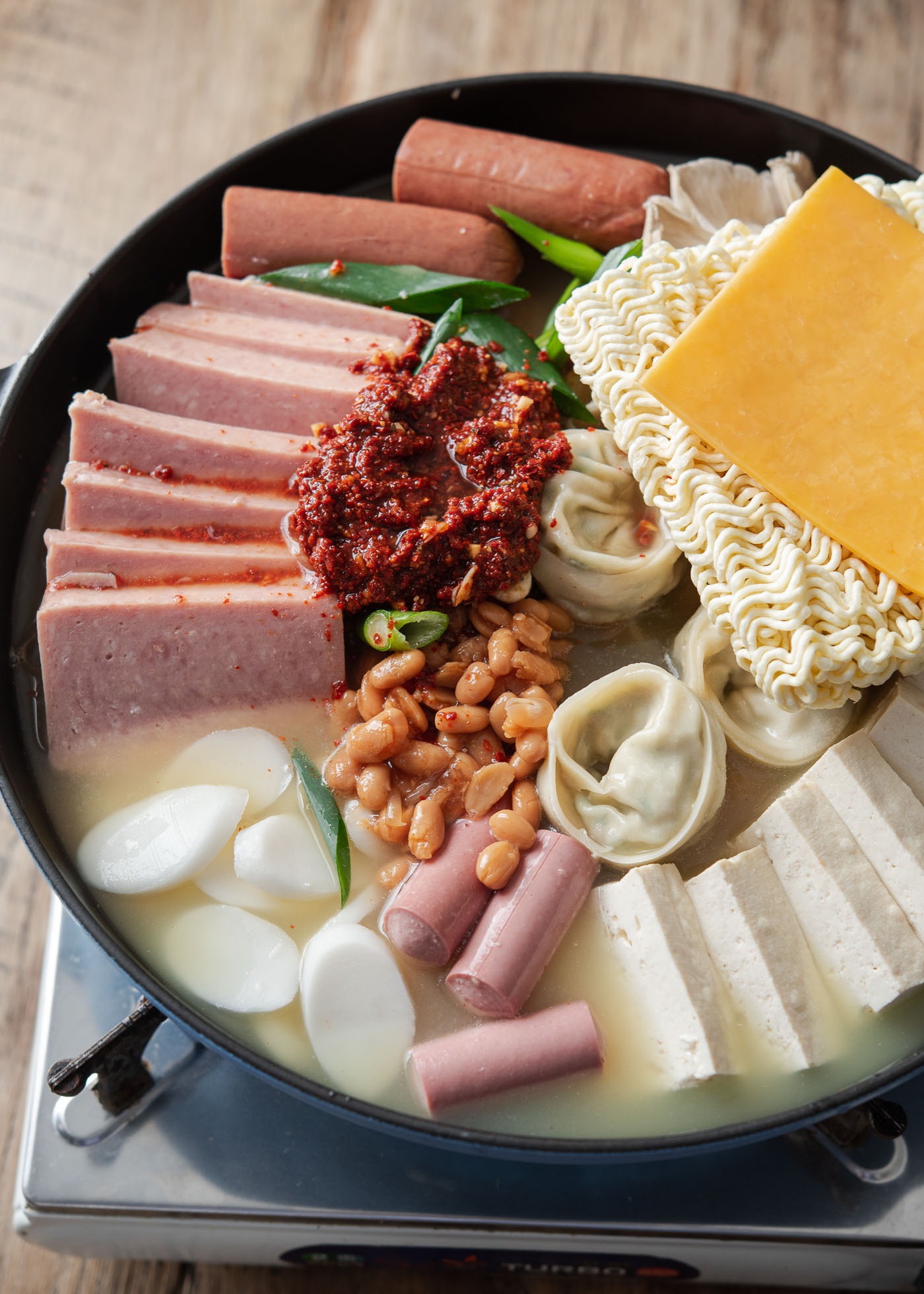 Korean army stew (budae jjigae) pot filled with canned meats, rice cakes, ramen noodles and cheese.