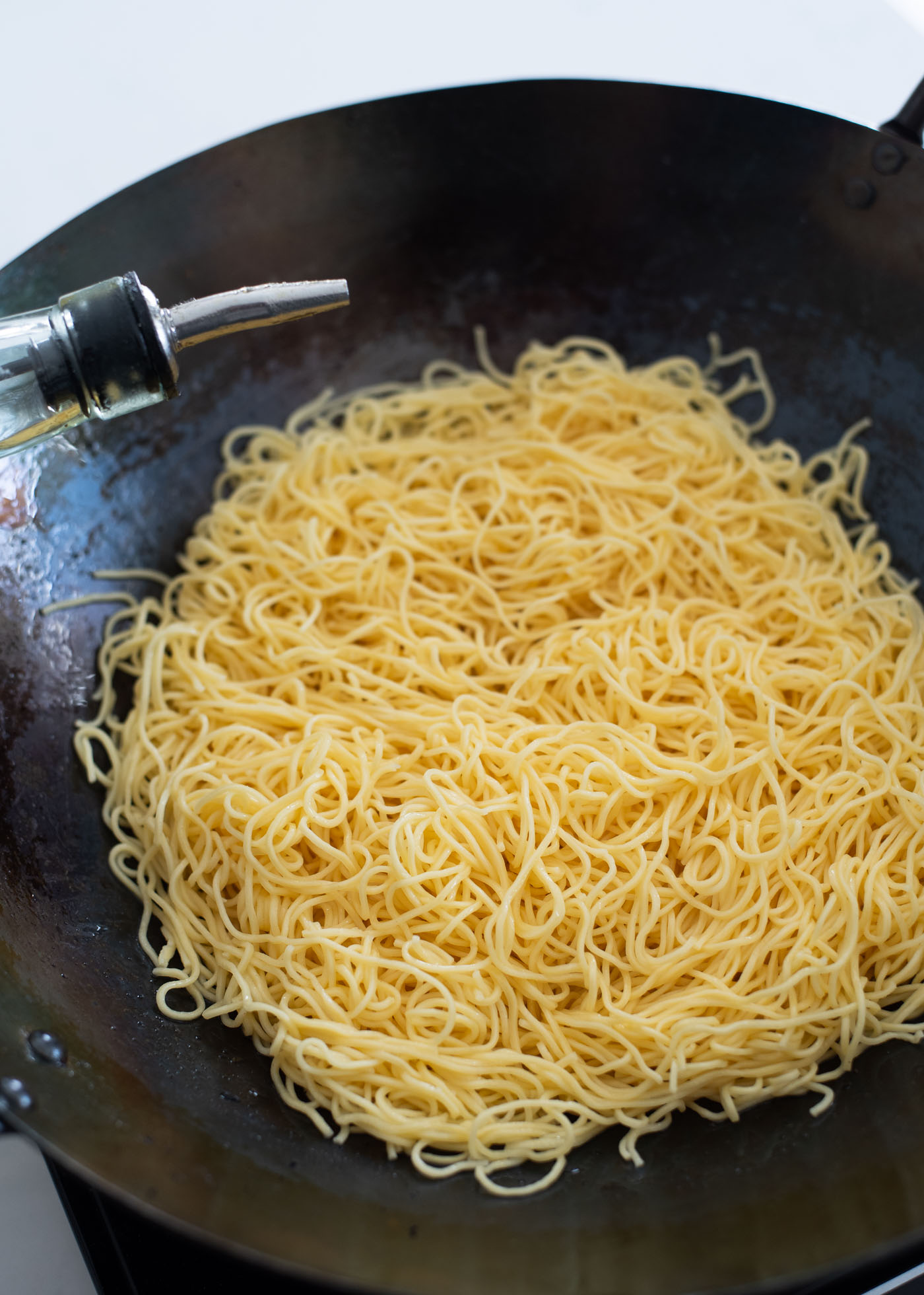 Cooked egg noodles are placed in a wok and oil is drizzled around,