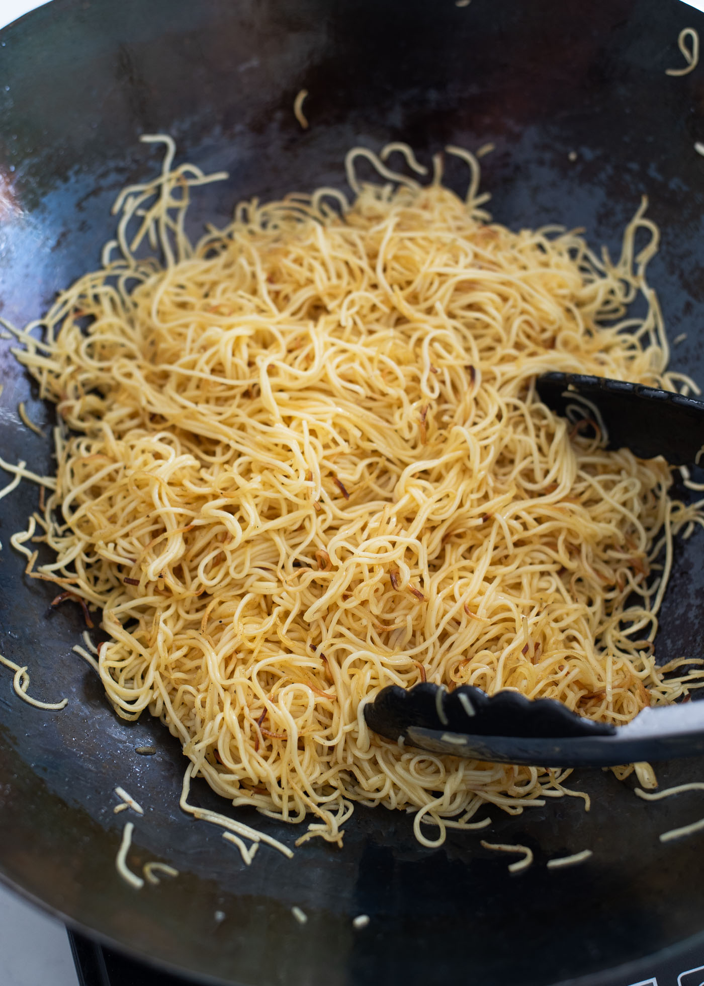 Kitchen tongs are stir frying the egg noodles to cook evenly.