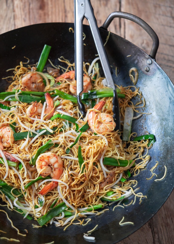 A wok filled with pan fried noodles with shrimp is showing.